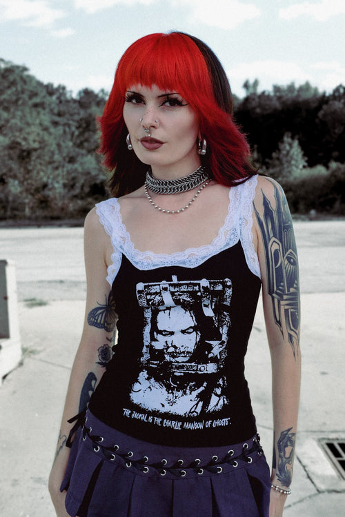 Woman with red hair and tattoos wearing a black tank top with graphic design outdoors.