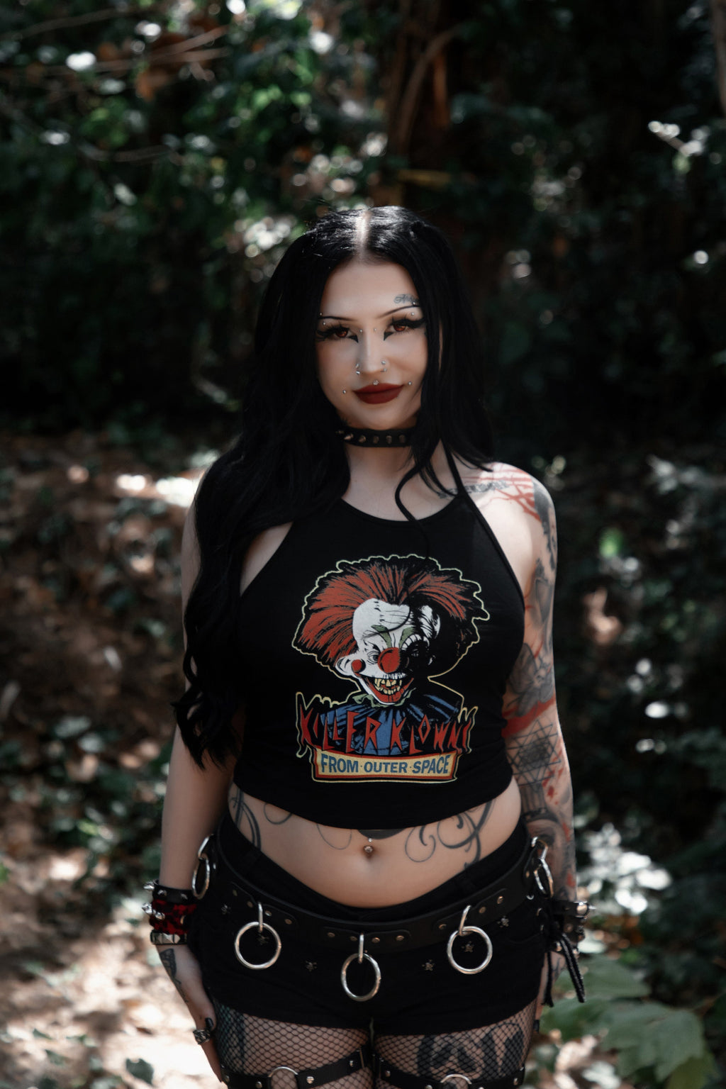 Person wearing a black crop top with a graphic design of Killer Klowns From Outer Space in a forest setting