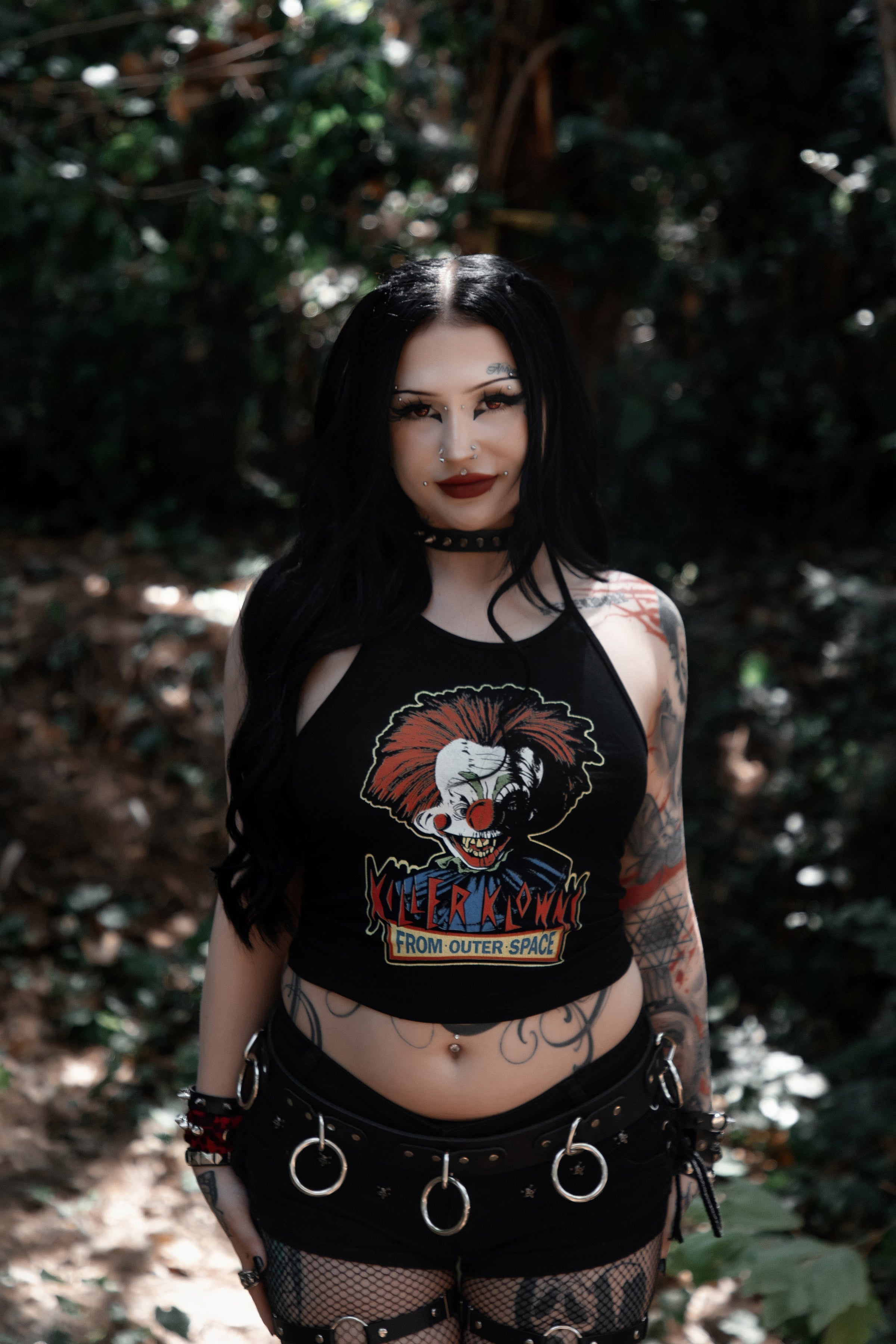 Person wearing a black crop top with a graphic design of Killer Klowns From Outer Space in a forest setting