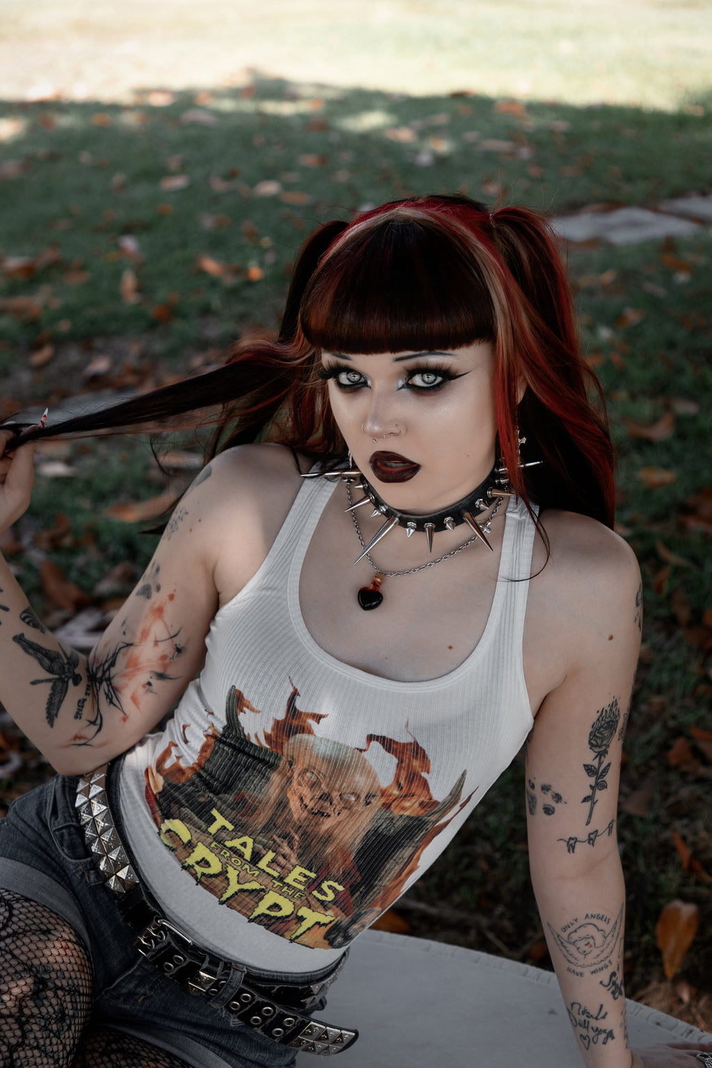 Person with tattoos and piercings wearing a white tank top with the Crypt-Keeper from 'Tales from the Crypt' graphic design outdoors.