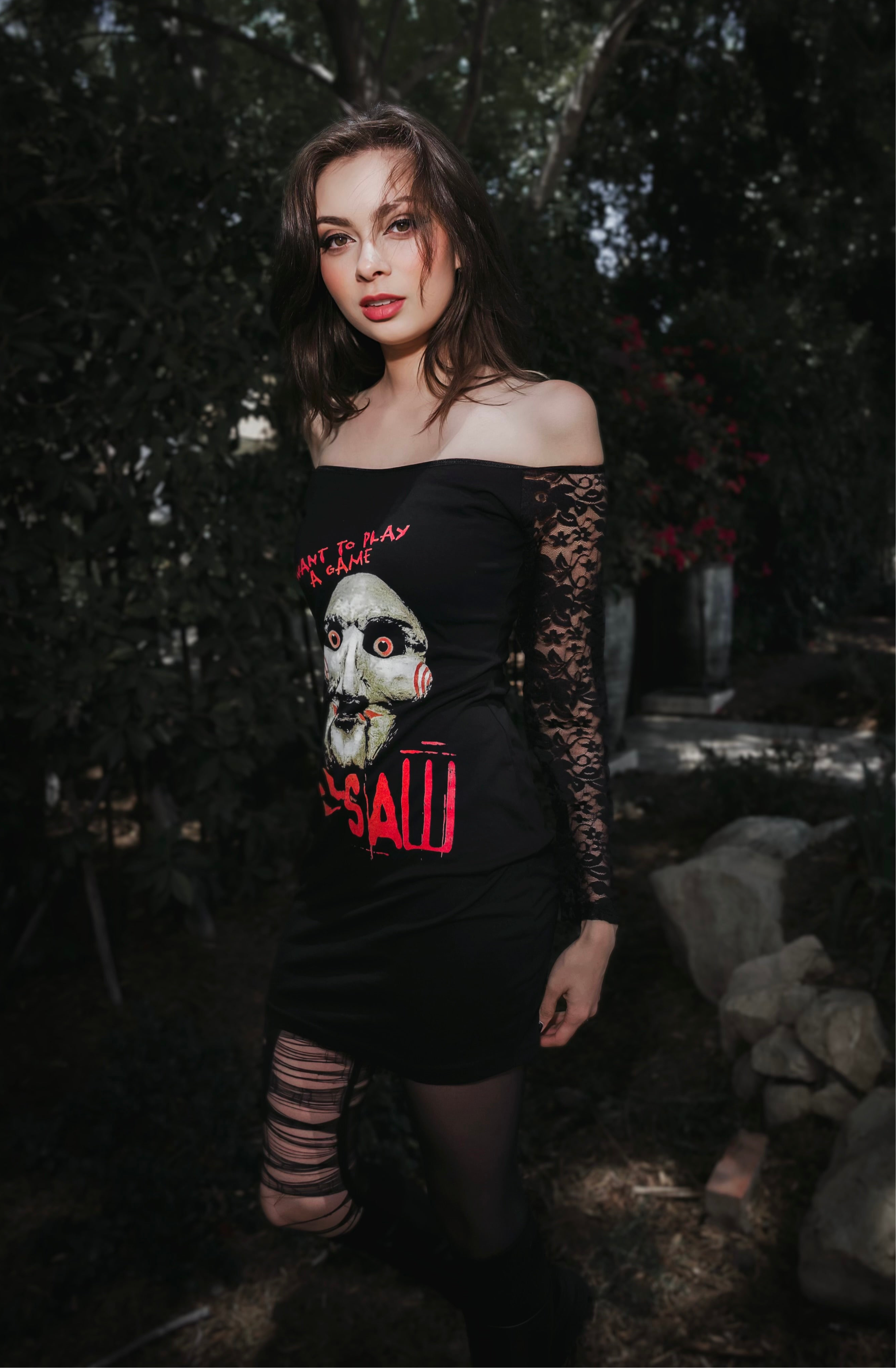 Woman wearing a black dress with a graphic design in a dark, outdoor setting