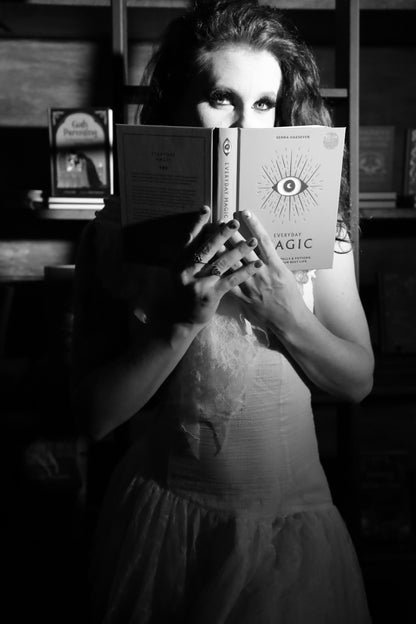 Person holding a book titled 'Everyday Magic' in a dimly lit room in front of the staircase of an old library shelf.