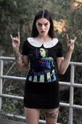 Person wearing a black dress with a colorful design, making a rock sign gesture outdoors.