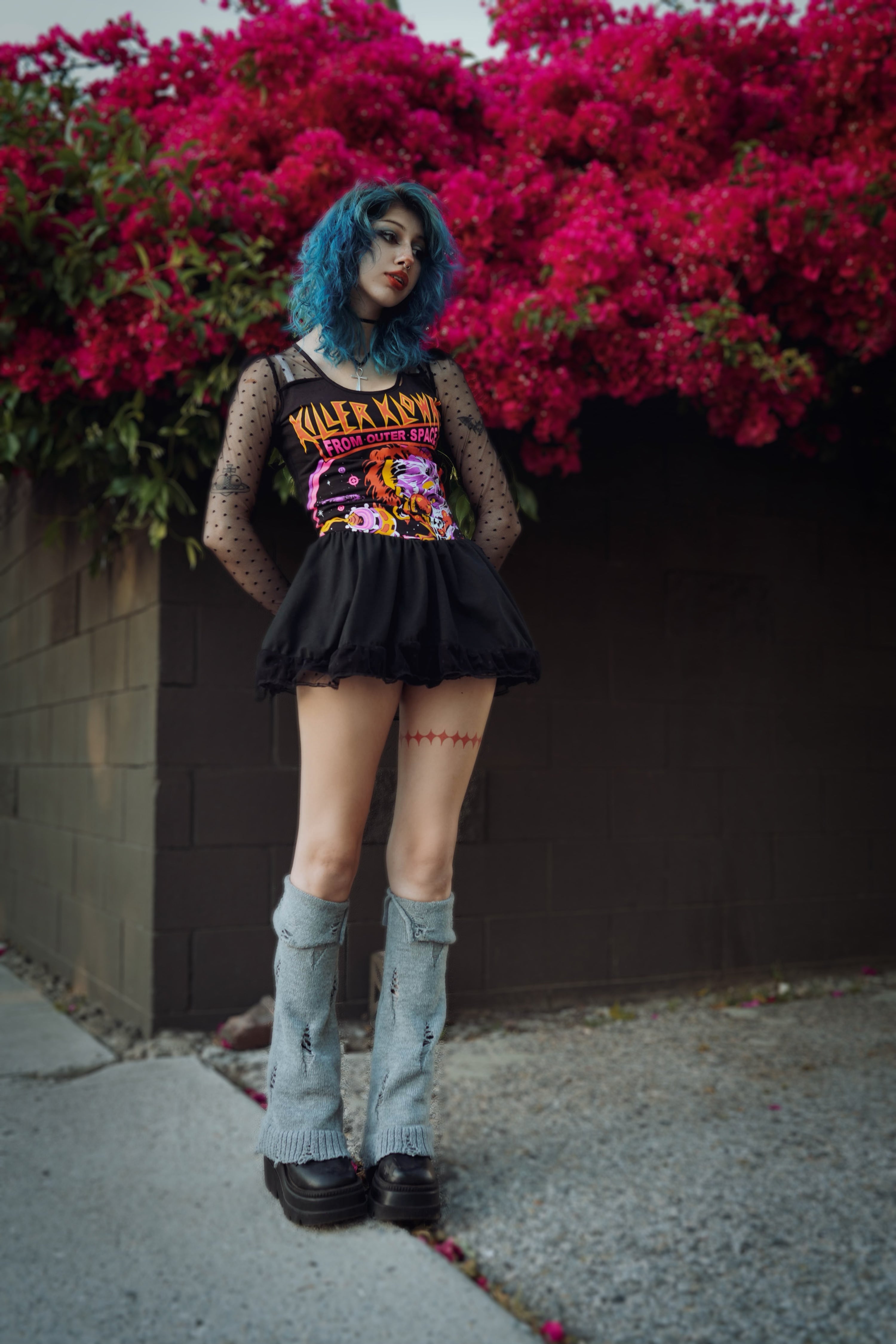 Person wearing a black outfit with colorful graphic t-shirt turned ballerina dress in front of red flowers